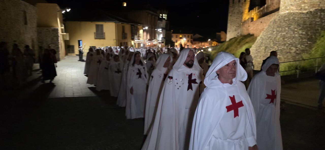 Desfile de personas con túnicas blancas y cruces rojas en la noche