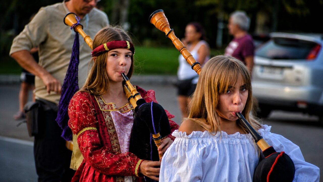 Niñas vestidas de época tocando instrumentos musicales en un desfile medieval