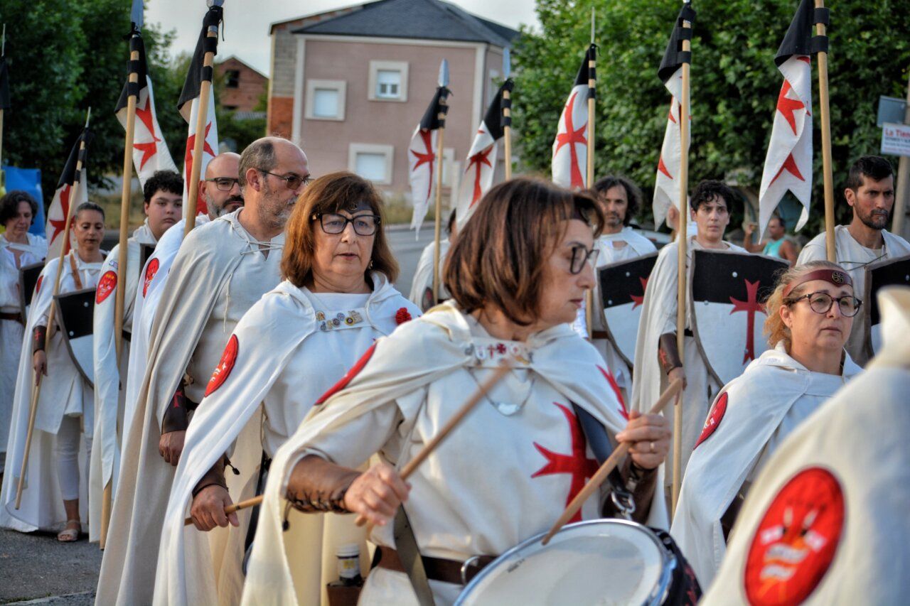 Grupo de personas vestidas con capas y escudos en un desfile medieval.