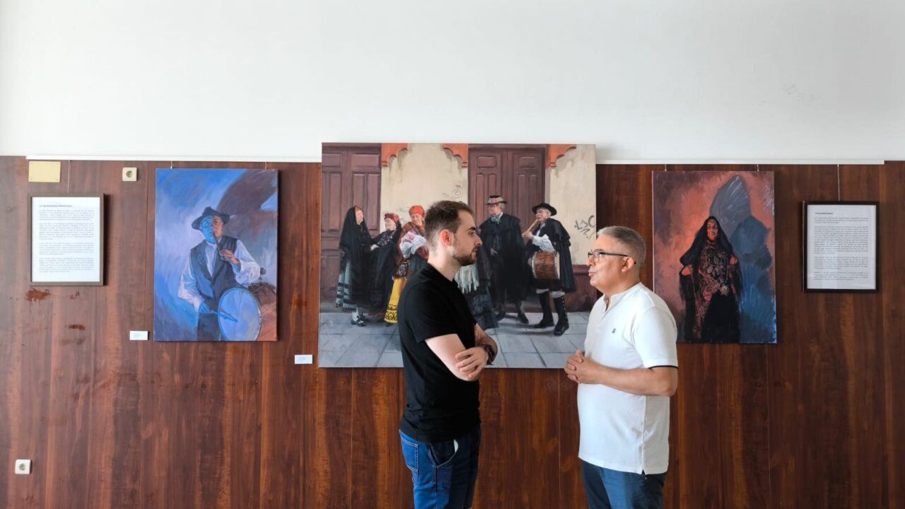 Dos personas conversando frente a pinturas en una exposición de arte.