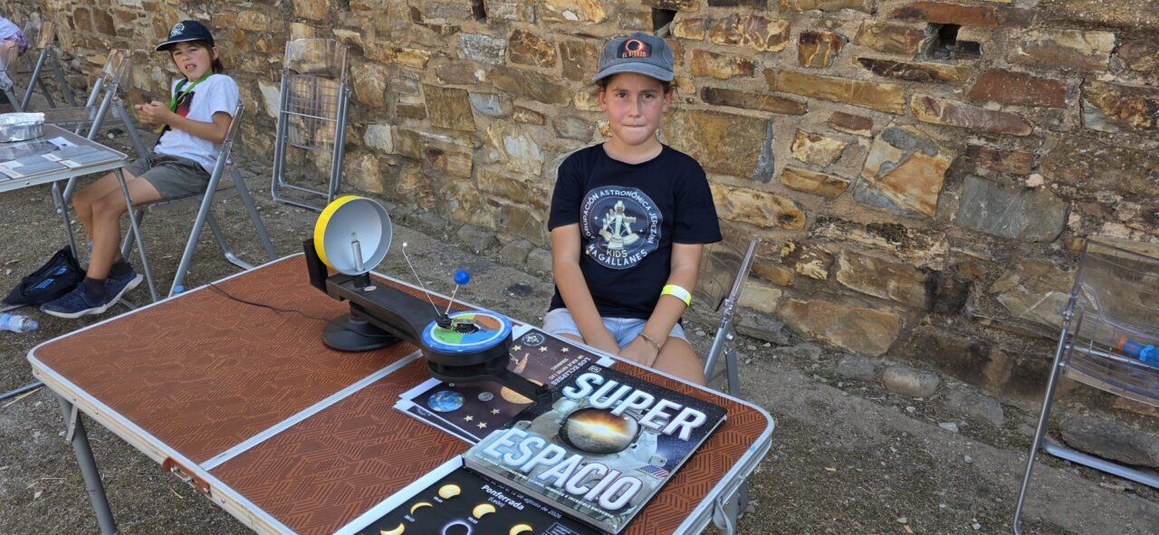 Niña sentada en una mesa con materiales sobre el espacio durante un eclipse solar
