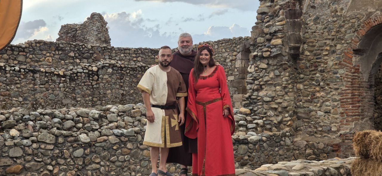 Tres personas vestidas con trajes medievales en el claustro del Monasterio de Carracedo