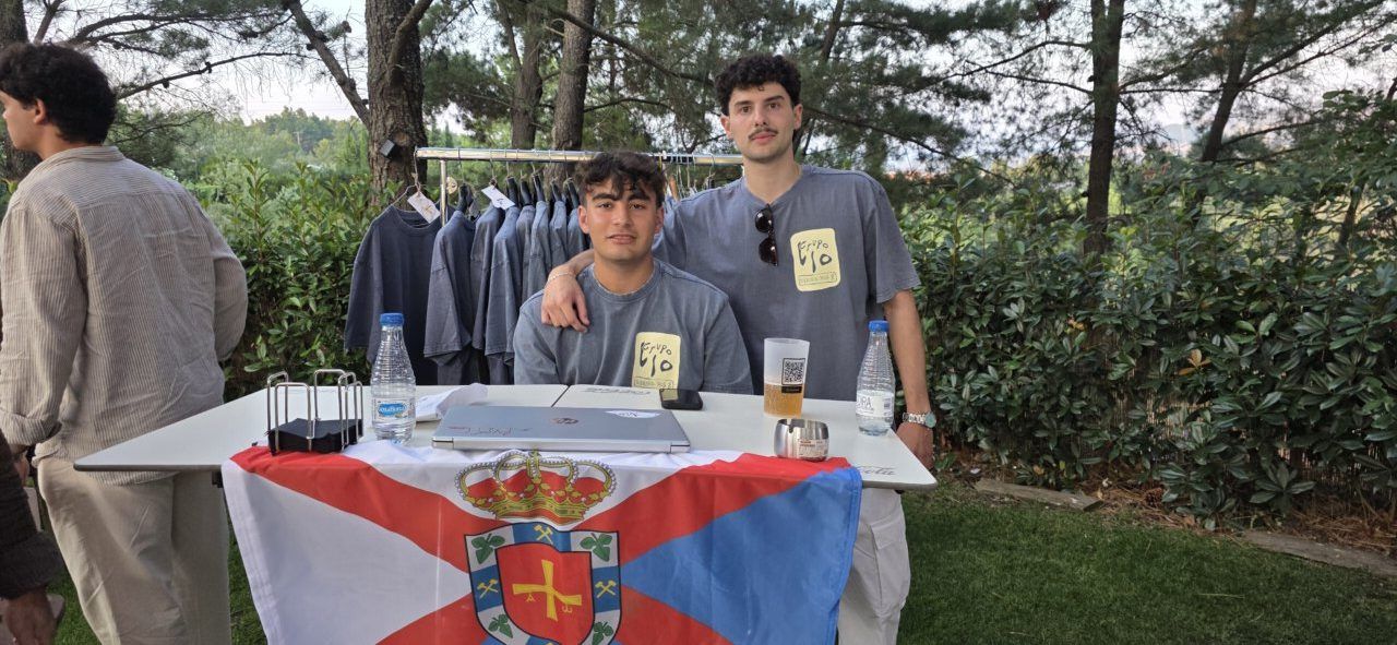 Dos jóvenes en una mesa con ropa y una bandera en un evento de música.