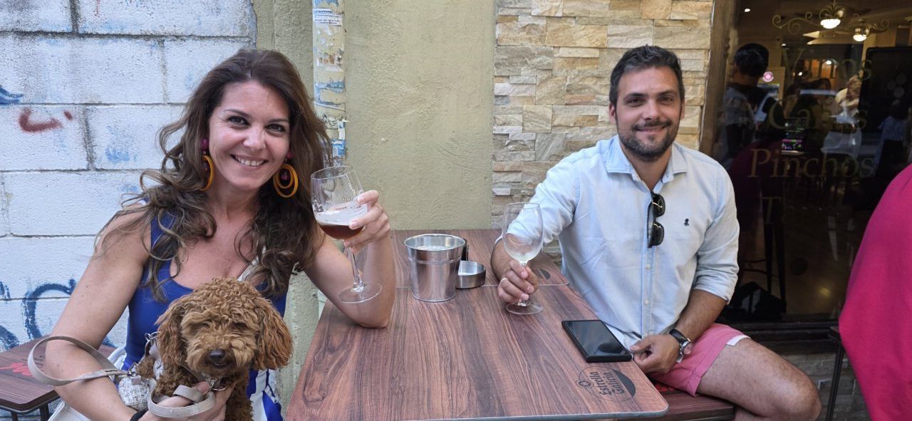Dos personas disfrutando de una bebida en una terraza con un perro