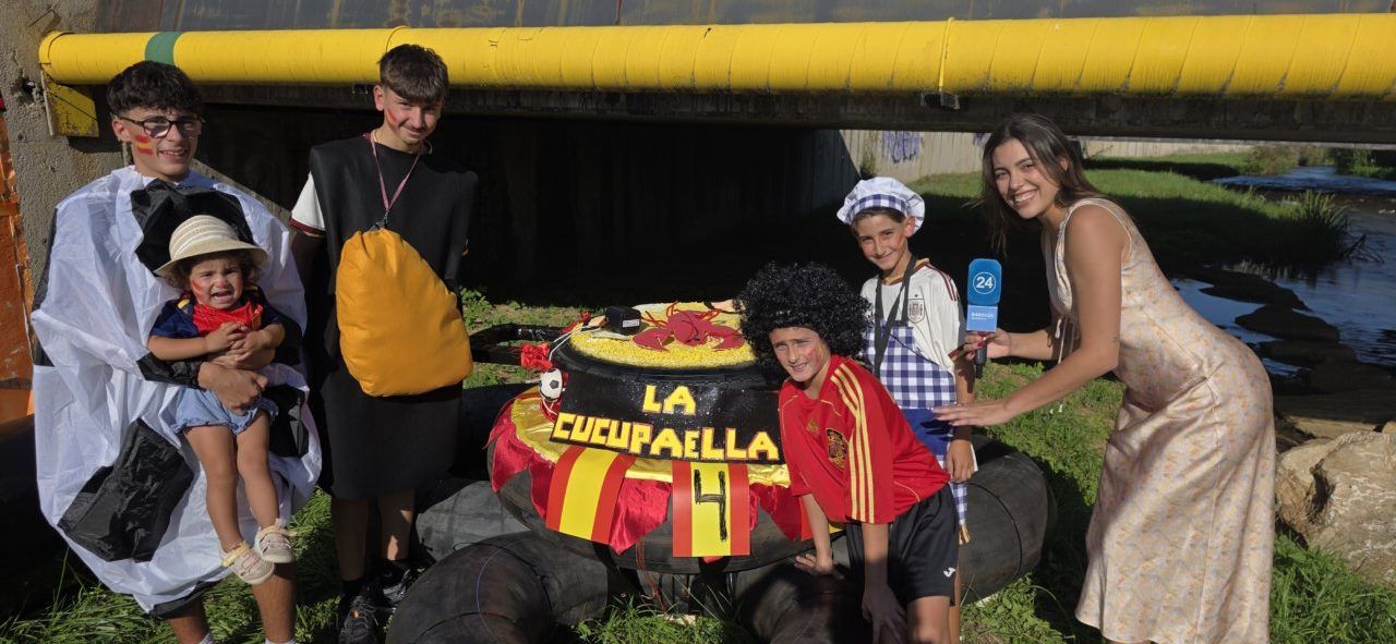 Grupo de niños y adultos en disfraces junto a una paella gigante