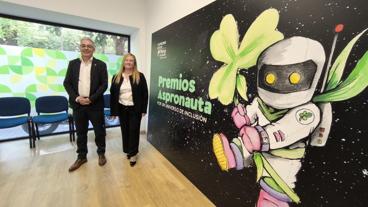 Dos personas posando frente a un mural de los Premios Aspronauta