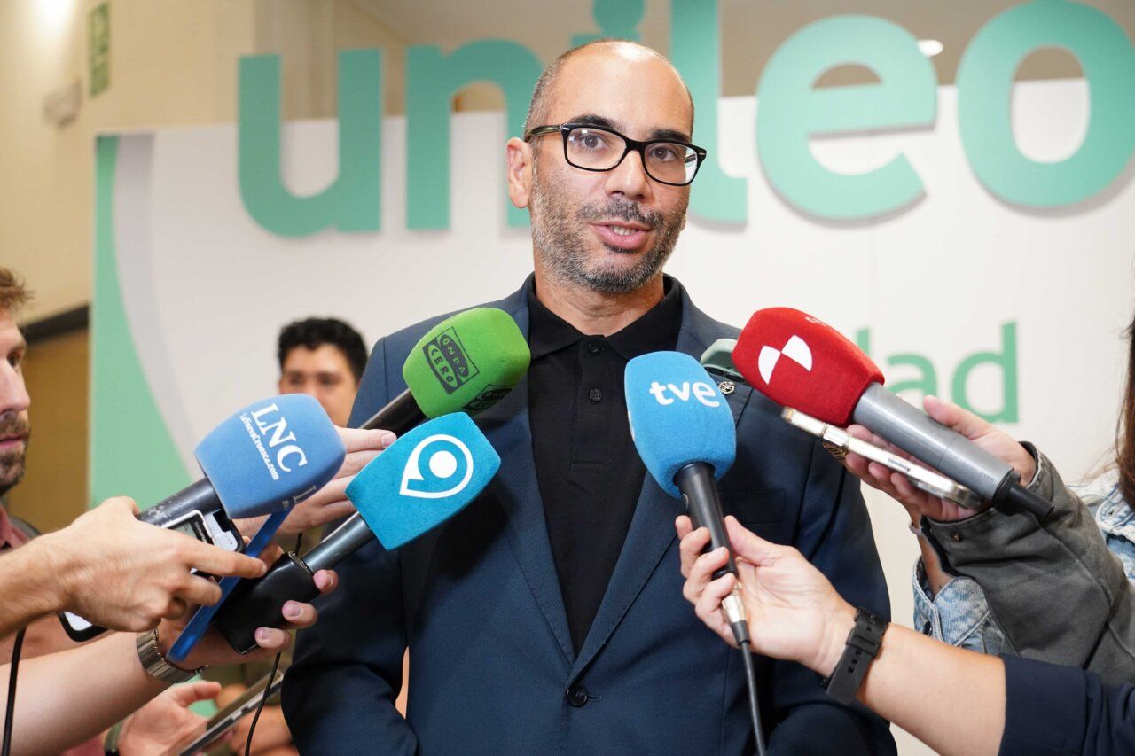 Un hombre hablando ante varios micrófonos en un evento de bienvenida