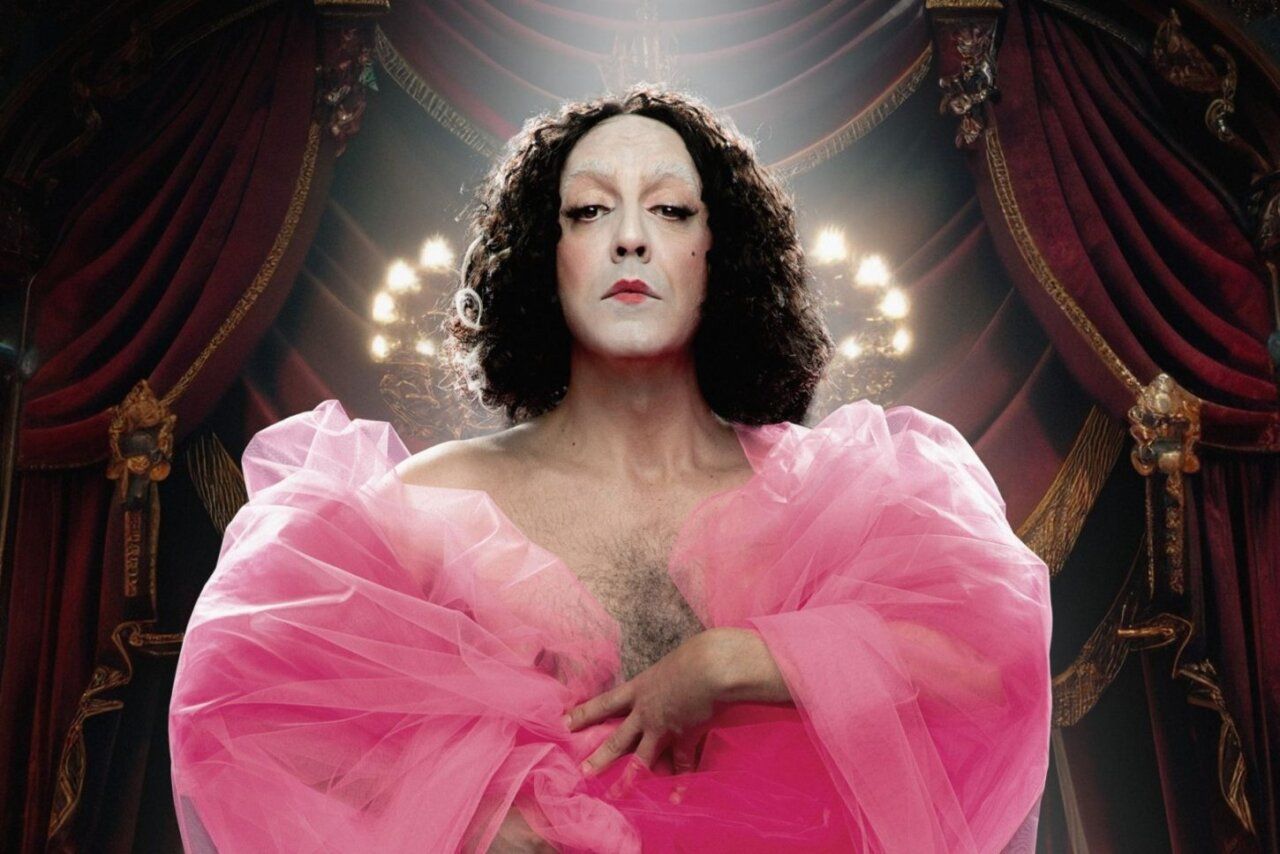 Actor en un vestido rosa con fondo teatral iluminado