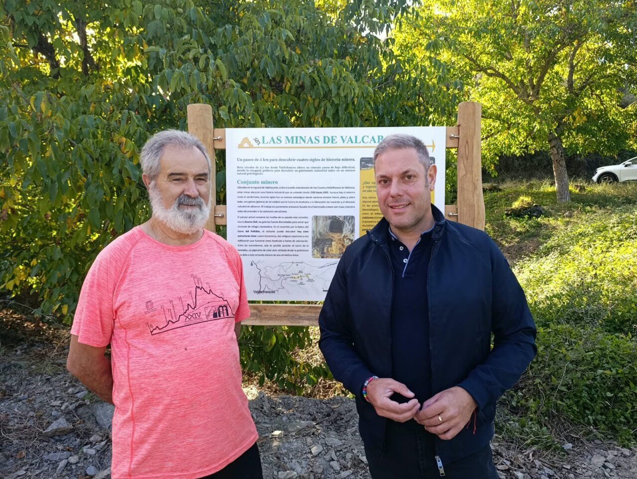 Dos hombres posando frente al cartel de las Minas de Valcabado.