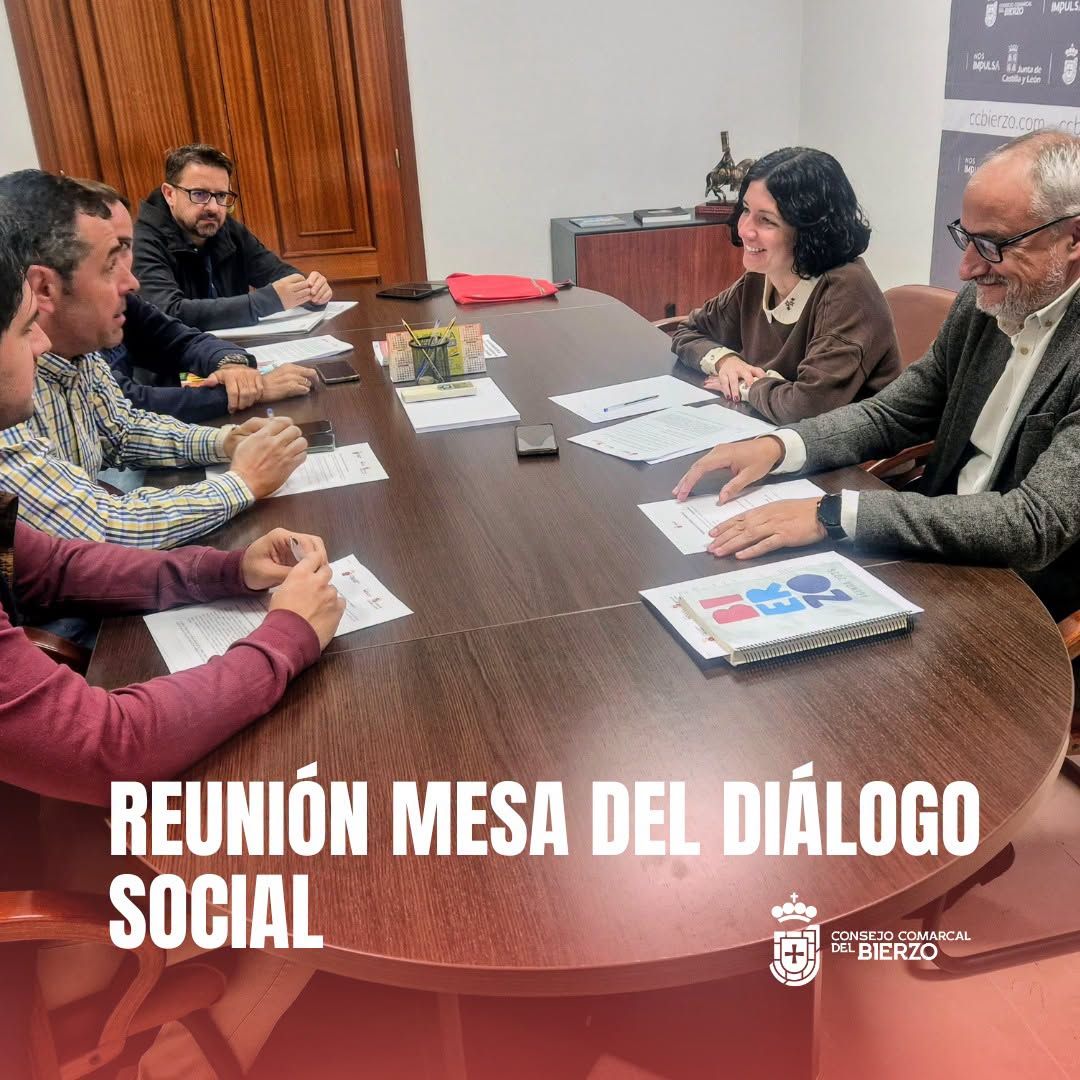 Varias personas se reúnen alrededor de una mesa con documentos en una sala.