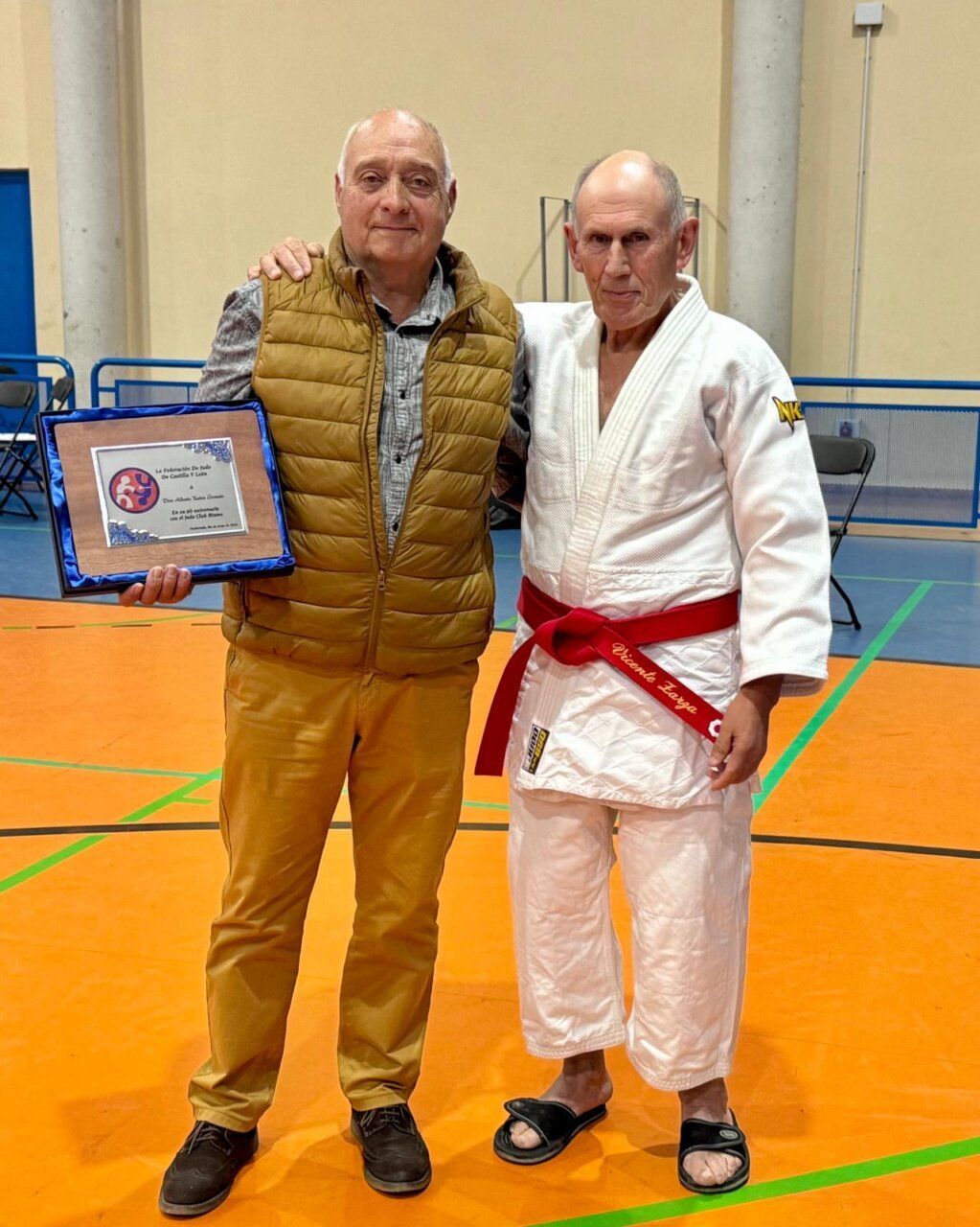 Dos hombres en un dojo sosteniendo un reconocimiento del Club Judo Blume.