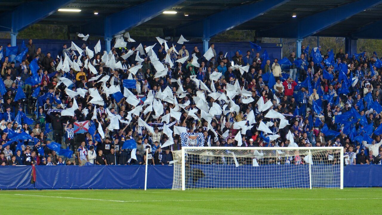 Aficionados en una grada ondean banderas azules y blancas detrás de una portería.