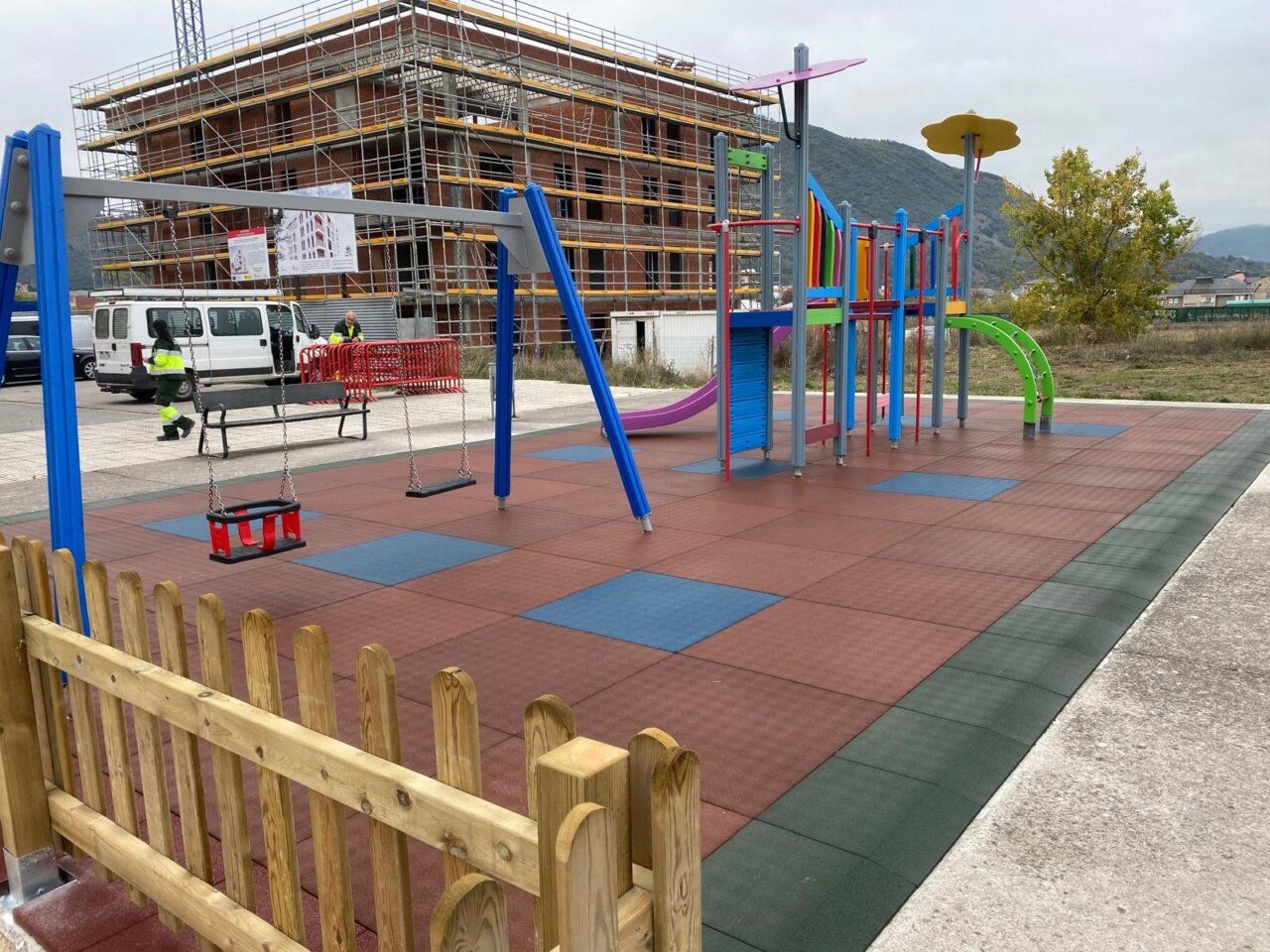 Área infantil con columpios y estructuras de colores junto a un edificio en obras
