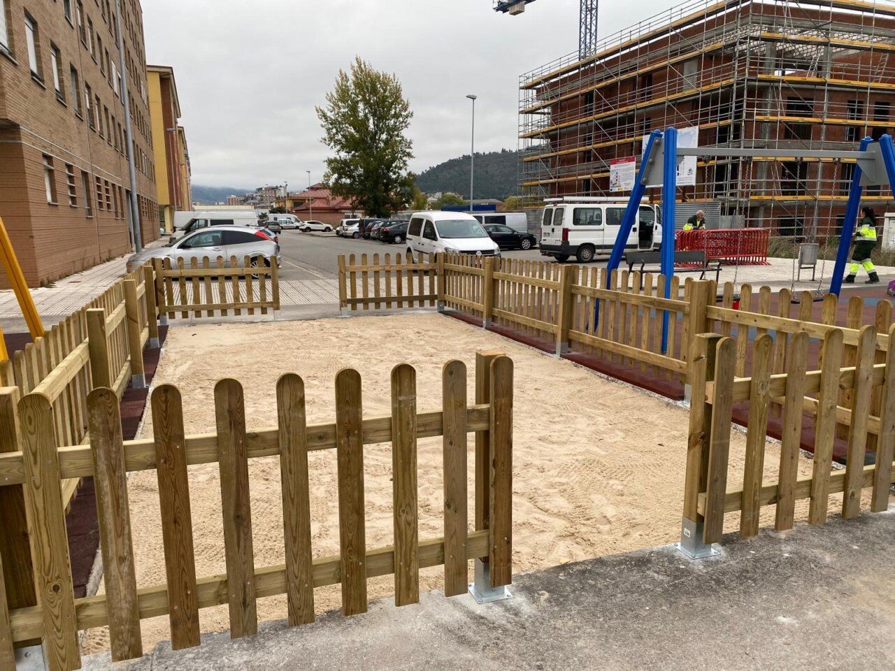 Zona infantil con arenero vallado de madera y columpio azul junto a obras
