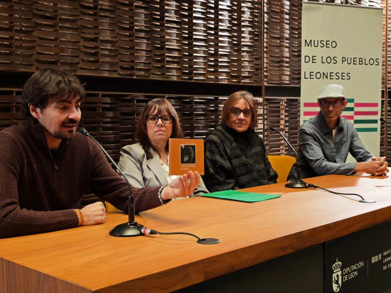 Cuatro personas sentadas ante una mesa; una sostiene un ejemplar del Cancionero Leonés.