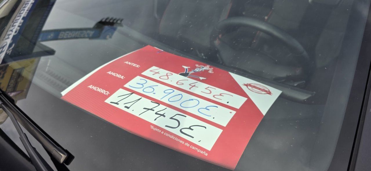 Cartel rojo con precios escritos a mano colocado tras el parabrisas de un coche.