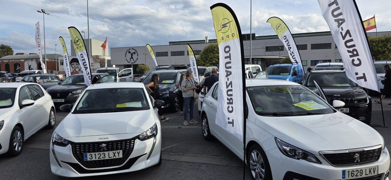 Varios coches estacionados en un recinto exterior, junto a banderolas publicitarias.