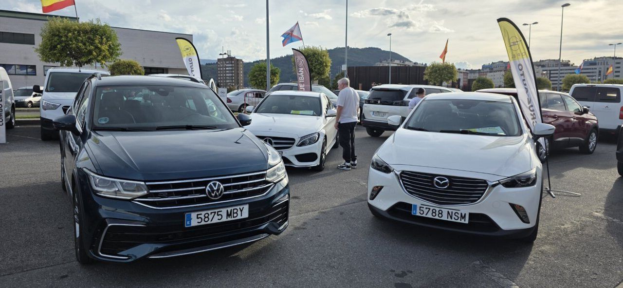 Varios coches estacionados en una exposición al aire libre, con un Volkswagen y un Mazda delante.