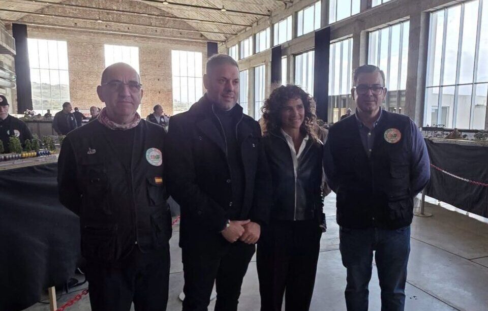 Cuatro personas posan junto a una maqueta ferroviaria en una amplia sala industrial.