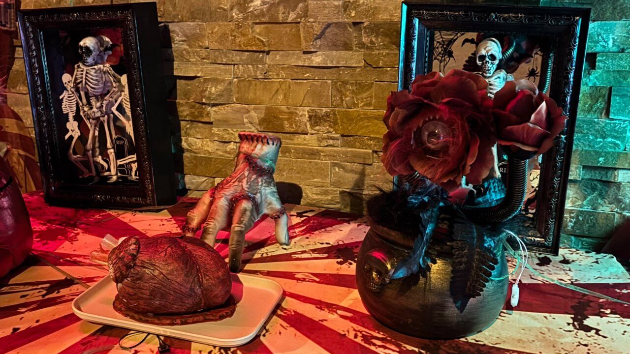 Decoración de Halloween con esqueletos enmarcados, una mano falsa y flores rojas.