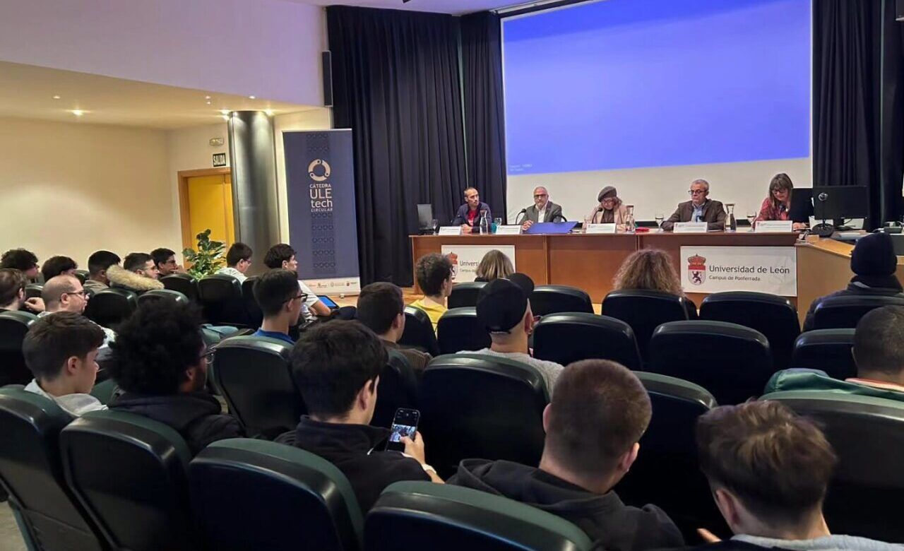 Público escucha a varias personas sentadas en una mesa durante una presentación.