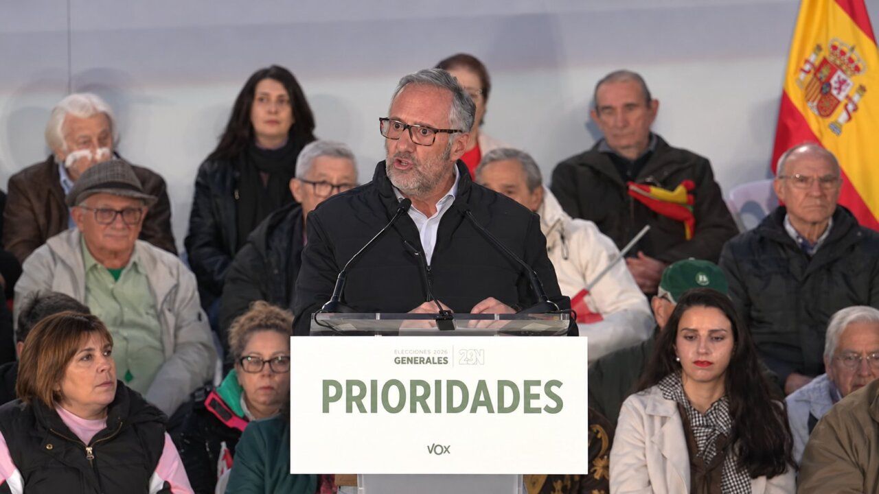 Un hombre habla ante un atril de Vox, con asistentes sentados y una bandera española.