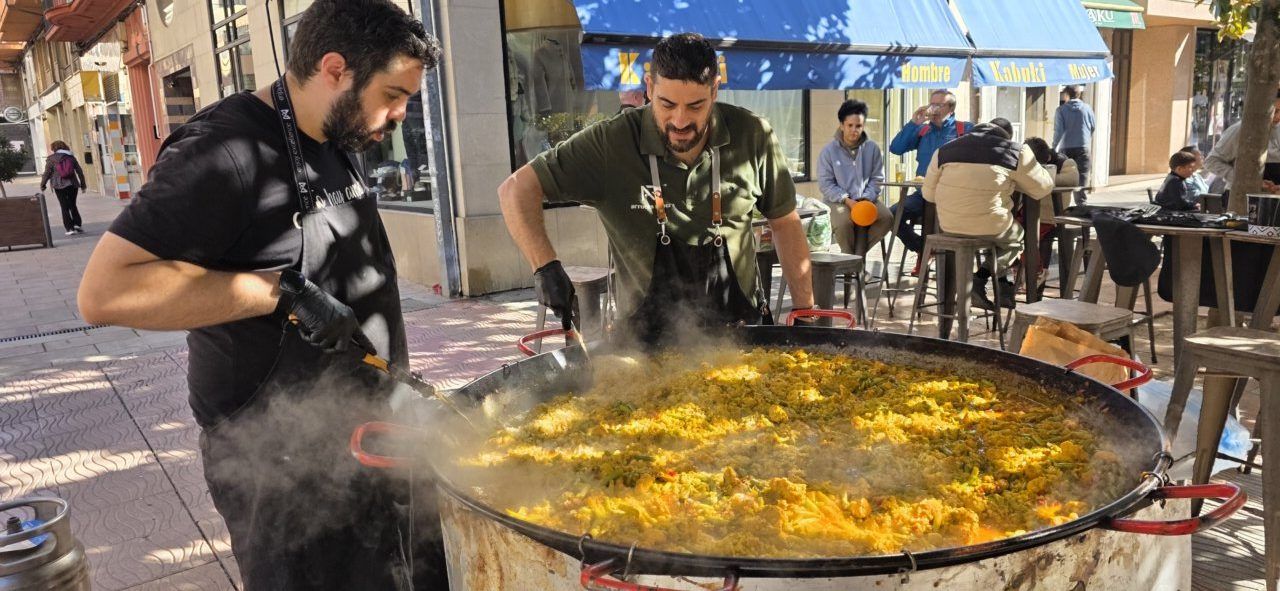 Dos hombres cocinan una gran paella en una sartén al aire libre