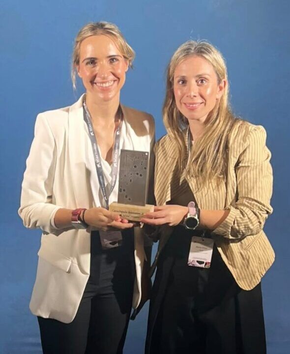 Dos mujeres sostienen una placa frente a un fondo azul.