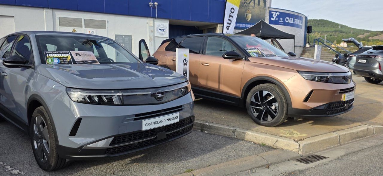 Dos vehículos Opel, uno gris y otro cobrizo, estacionados junto a un edificio.