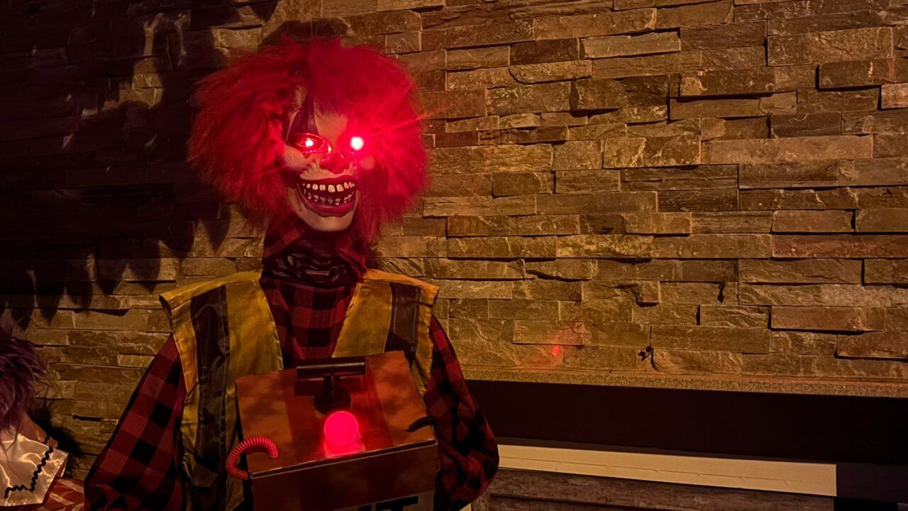 Figura de payaso siniestro con peluca roja y ojos iluminados junto a una caja