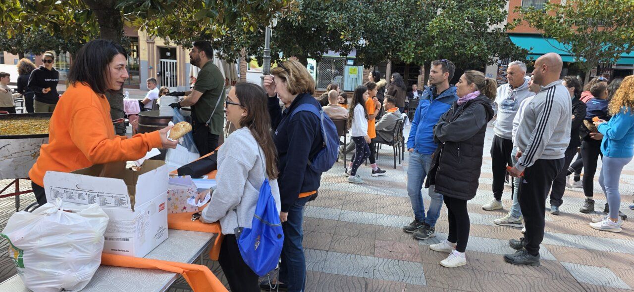 Personas esperan junto a una mesa mientras una mujer entrega una pieza de pan.