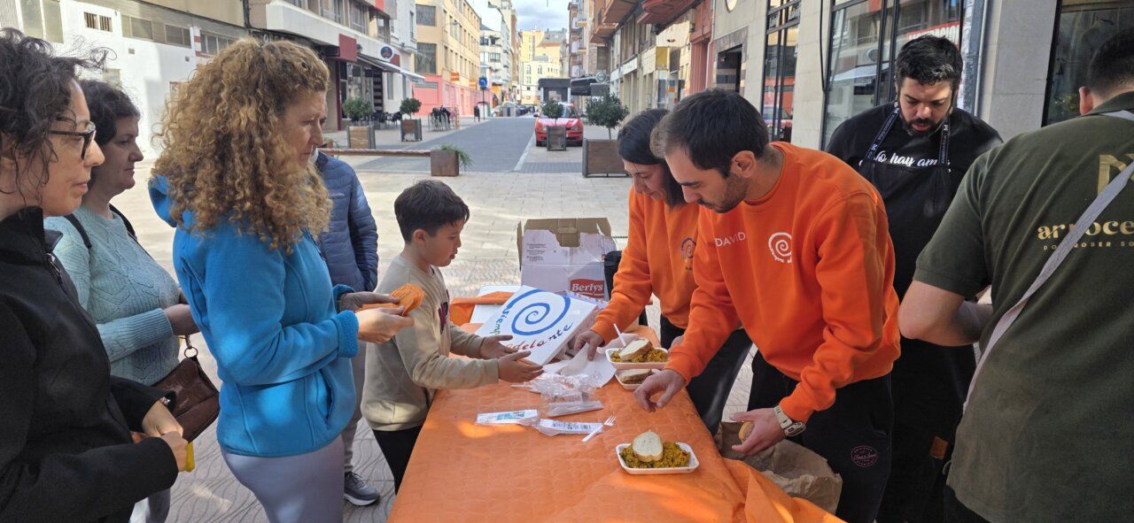 Personas se reúnen alrededor de una mesa y comparten comida en una calle peatonal.