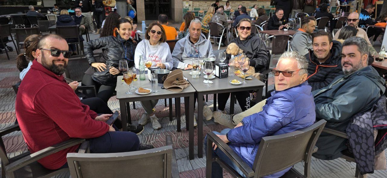Varias personas sentadas alrededor de mesas al aire libre con bebidas y platos.