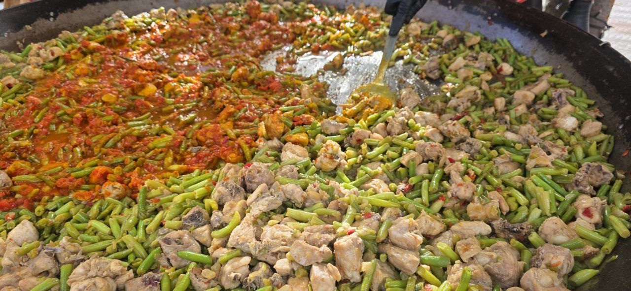 Primer plano de una gran paella con judías verdes, carne y verduras.