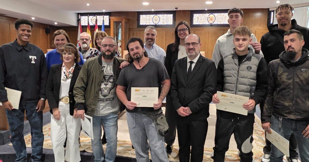 Grupo de personas posa con certificados en una sala de madera del ayuntamiento.