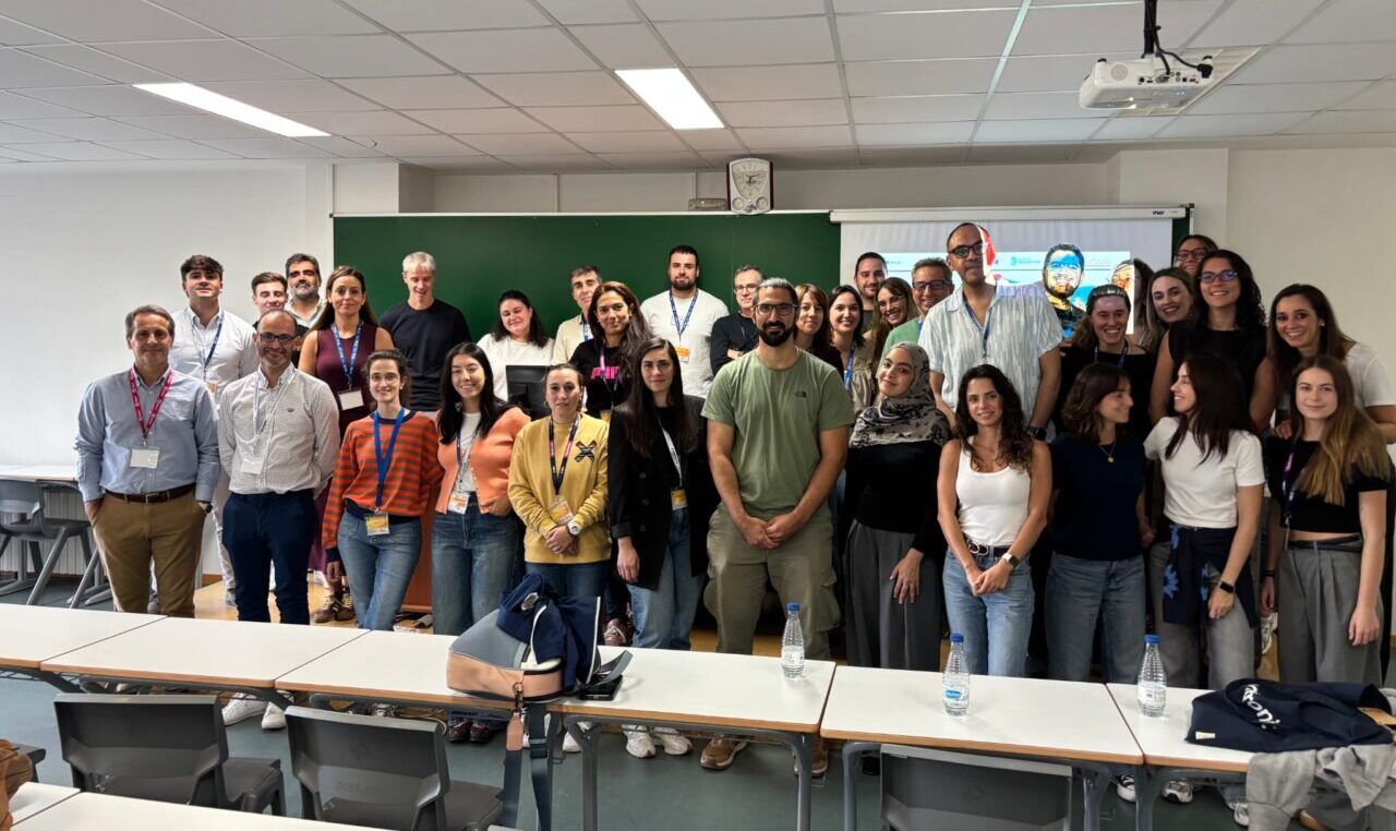 Grupo numeroso posa en un aula frente a una pizarra y una pantalla de proyección.
