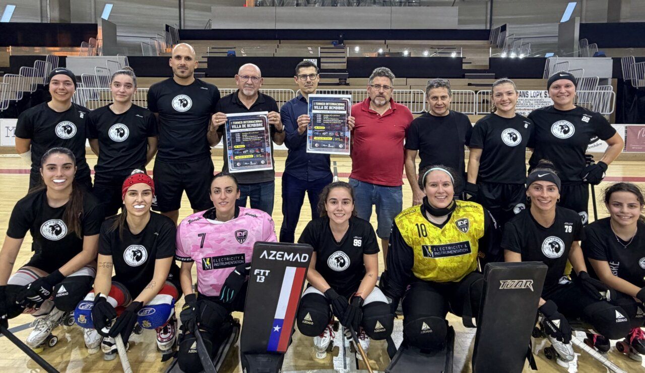 Jugadoras de hockey sobre patines y varios hombres posan con carteles en una pista cubierta.
