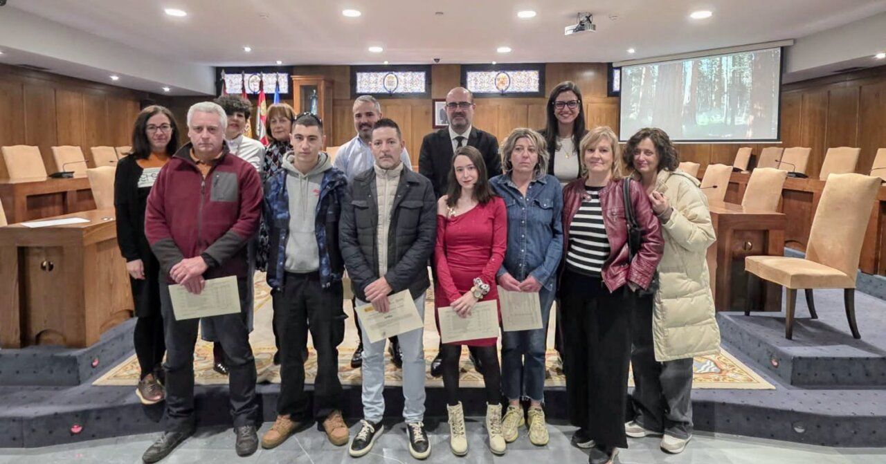 Grupo de personas posa con certificados en una sala de plenos municipal.