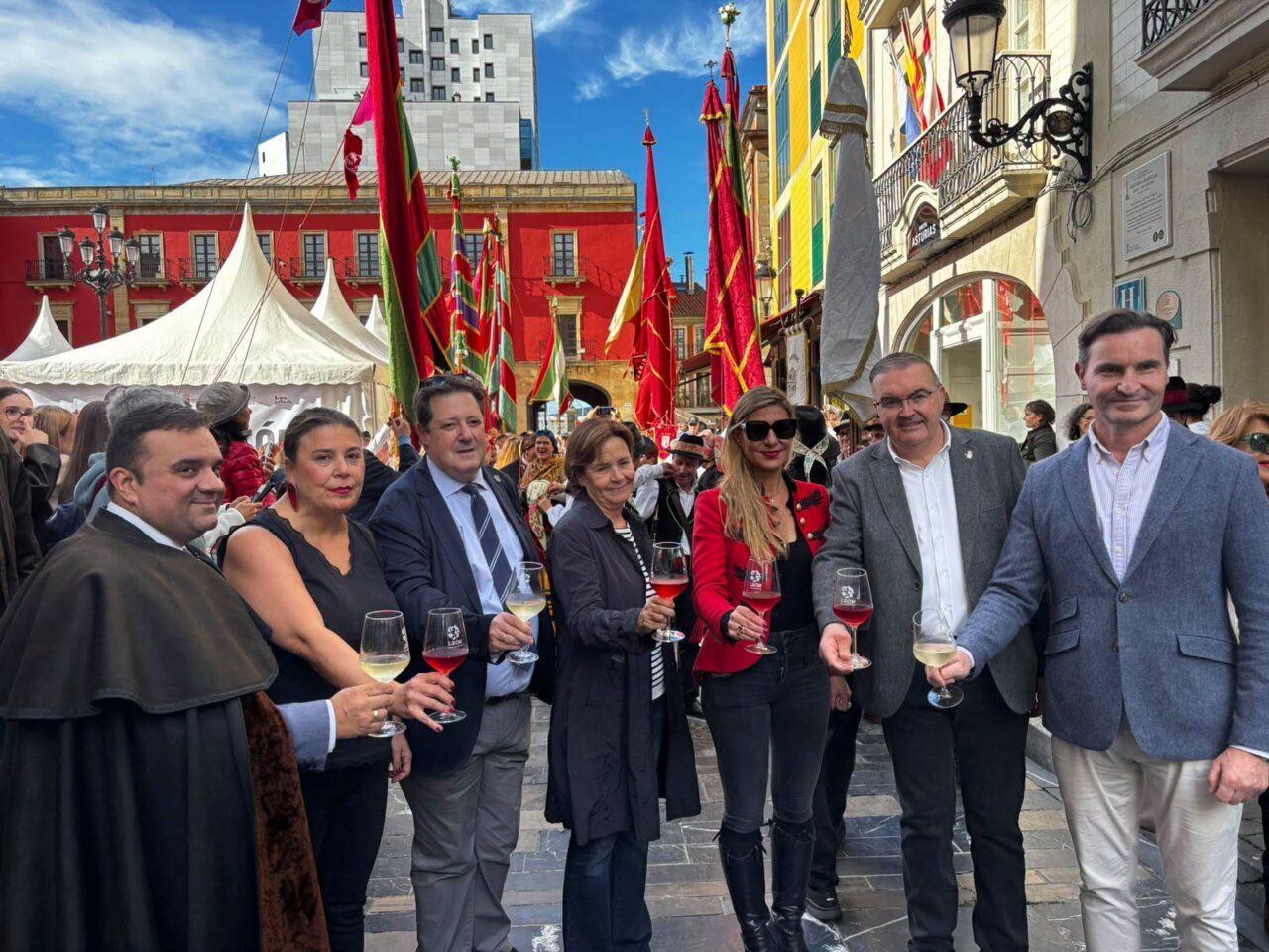 Un grupo posa con copas bajo pendones en una calle con puestos de feria