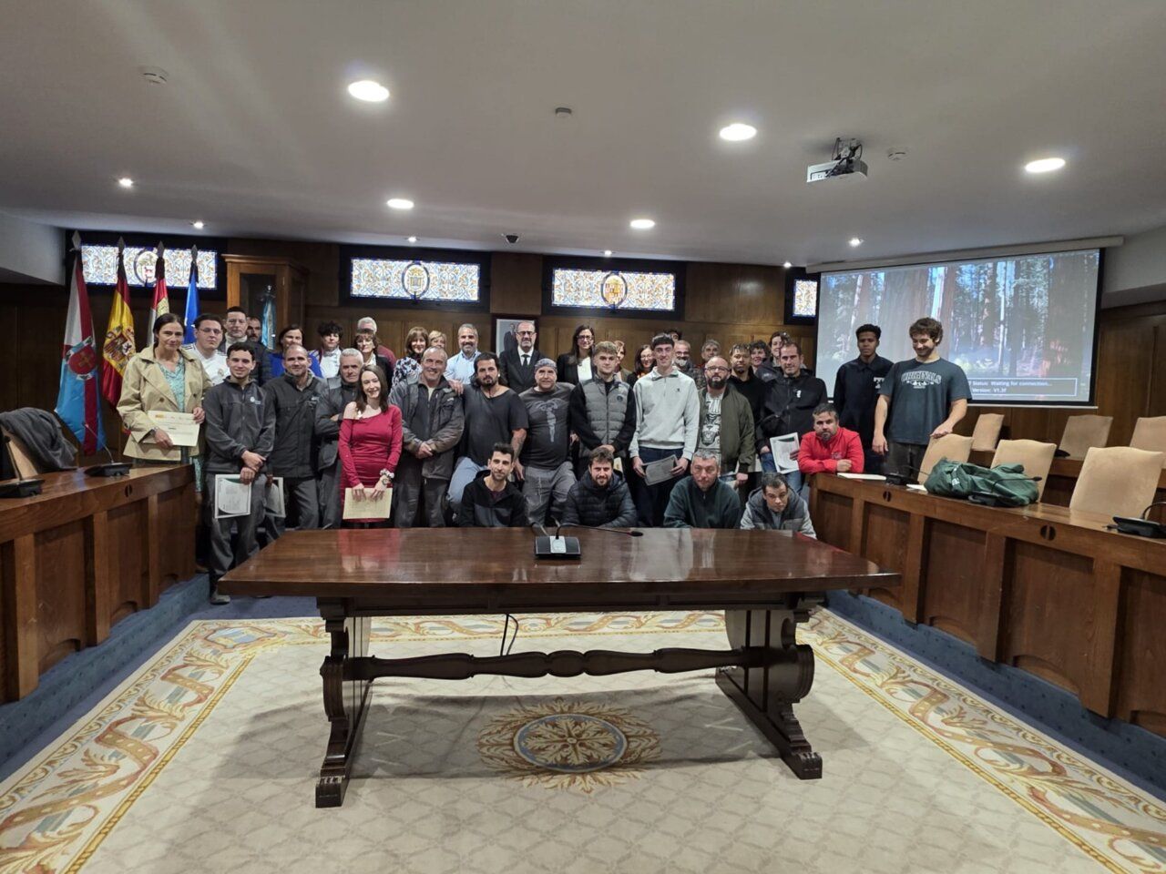 Grupo de personas posa en una sala institucional; varias sostienen documentos.