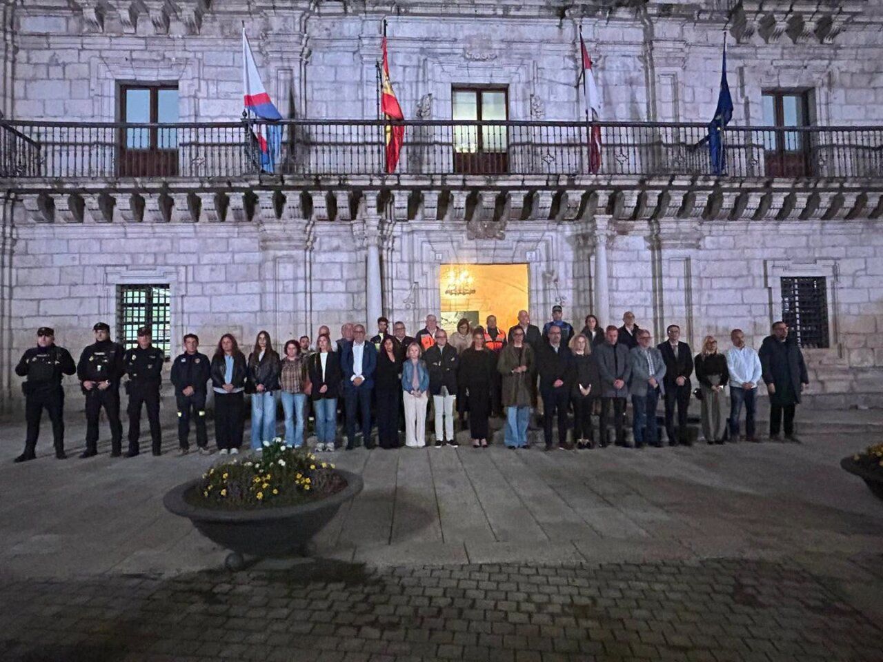 Grupo de personas frente a un edificio de piedra con varias banderas