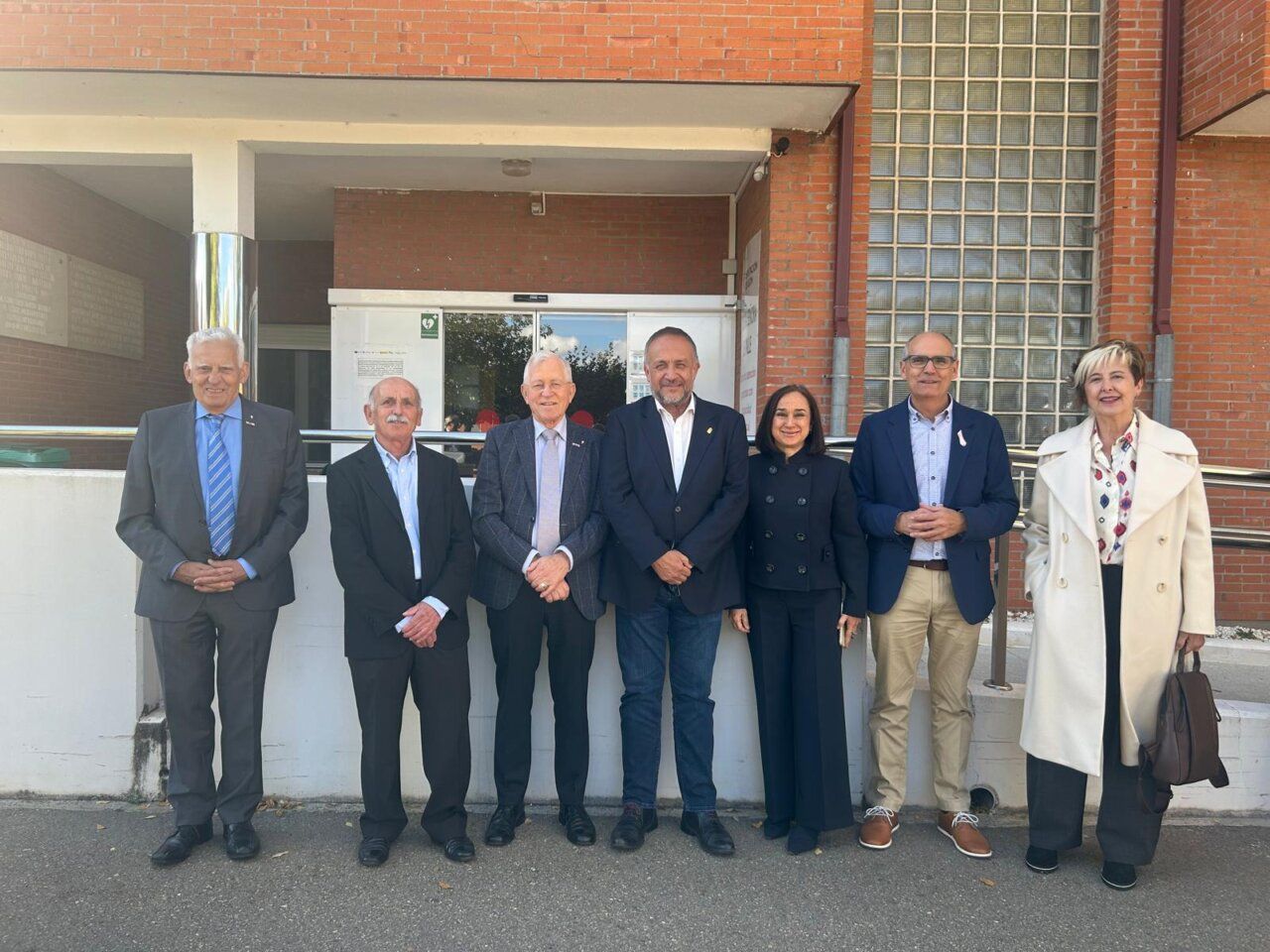 Siete personas posan frente a la entrada de un edificio de ladrillo.