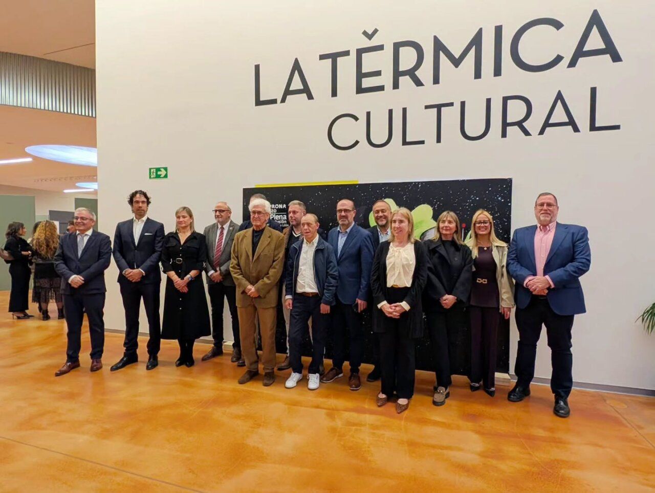 Grupo de personas posa frente a un panel en un espacio cultural.