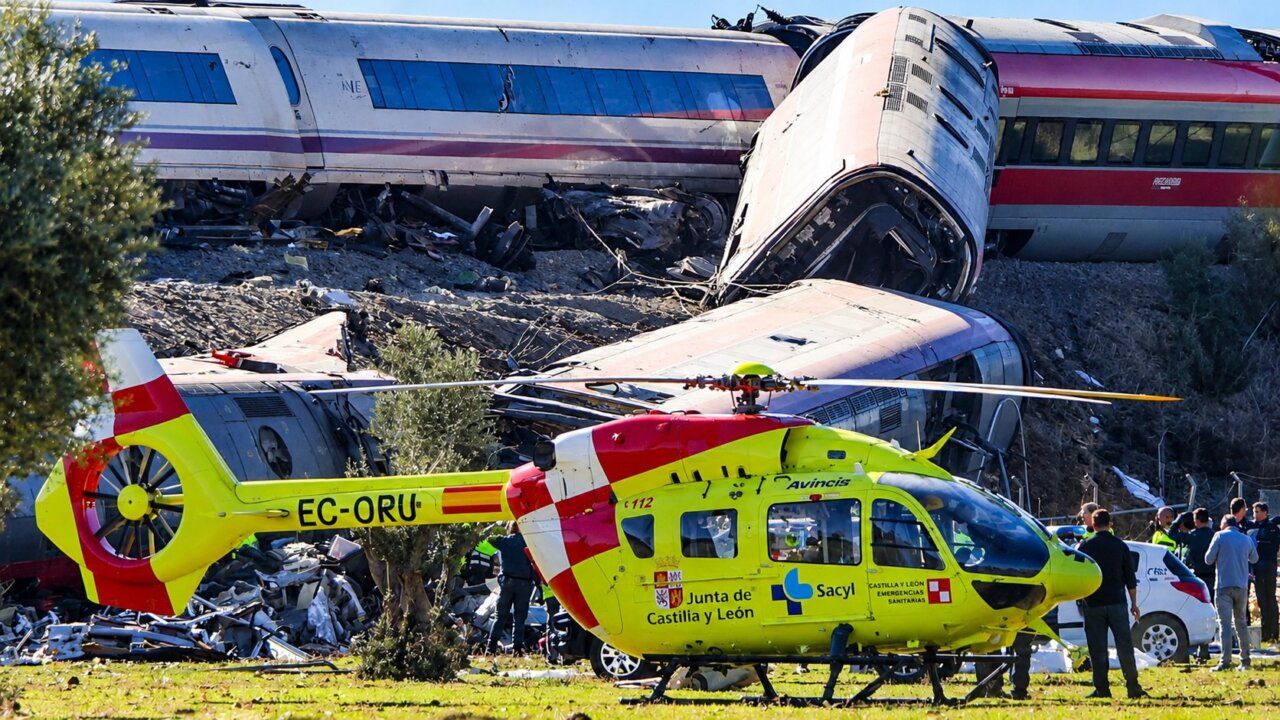 Un helicóptero amarillo está junto a varios vagones descarrilados y personas en el lugar
