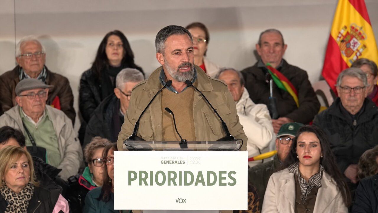 Un hombre habla ante un atril de Vox, con público y una bandera española detrás.