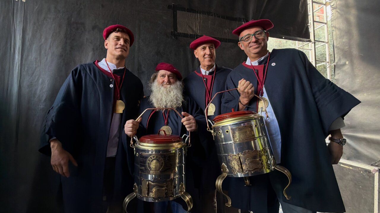 Cuatro hombres con boinas rojas posan junto a dos ollas ferroviarias metálicas