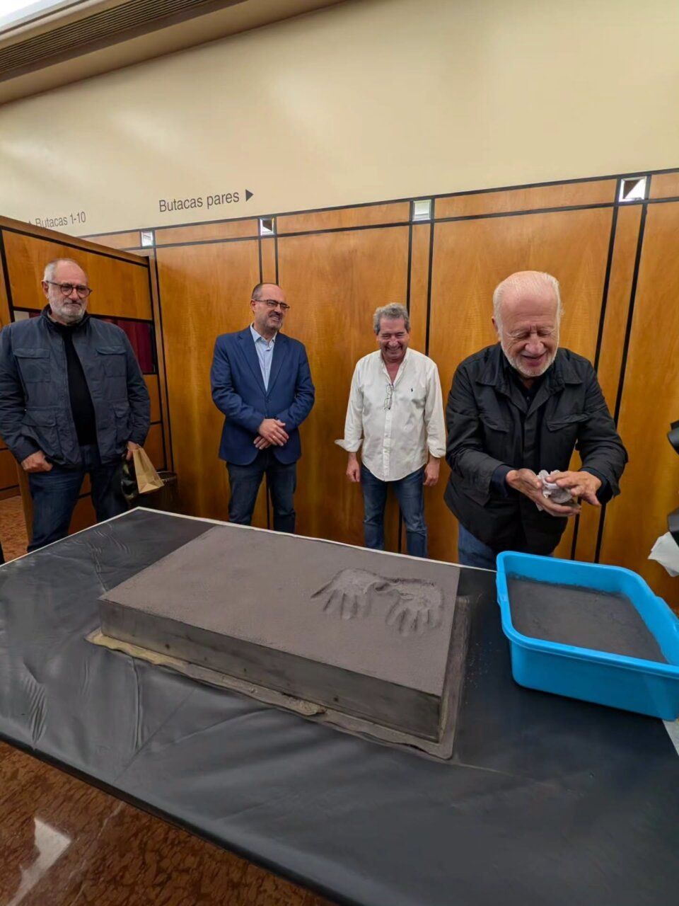 Cuatro hombres se reúnen alrededor de una placa con impresiones de manos.