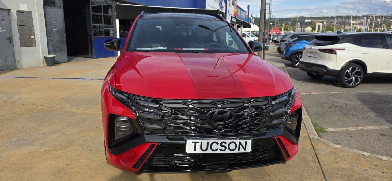 Hyundai Tucson rojo visto de frente, estacionado junto a otros vehículos en exposición.