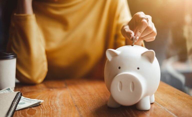 Persona depositando monedas en una alcancía en una mesa de madera