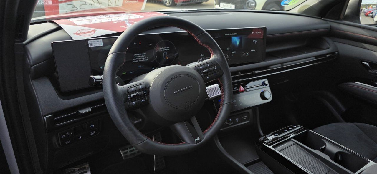 Interior de un automóvil con volante, pantallas digitales y consola central.